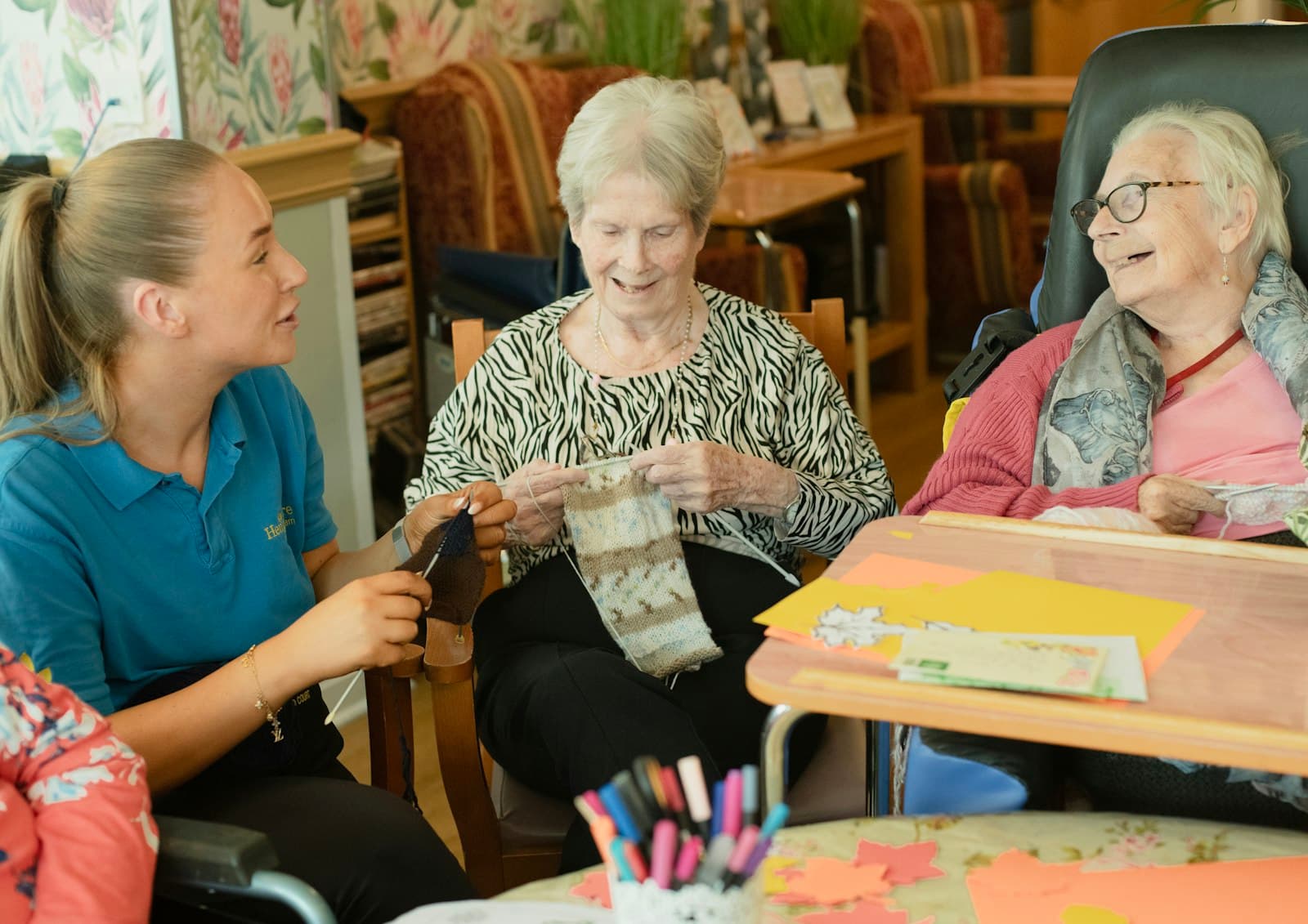 A carer sitting and chatting with two older women as they knit together